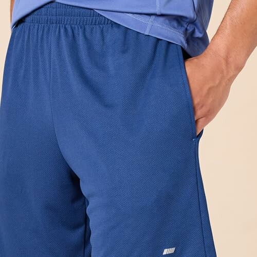 Person wearing blue athletic shorts with hand in pocket.