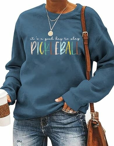 Person wearing blue sweatshirt with 'Pickleball' text and holding a coffee cup.