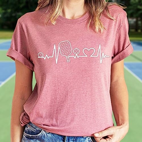 Woman wearing a pink t-shirt with pickleball heartbeat design.