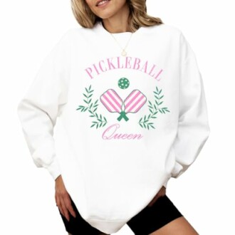 Woman wearing white sweatshirt with 'Pickleball Queen' design featuring paddles and leaves.